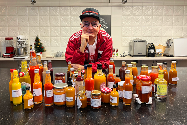 Le Hot Sauce Lord posant devant une multitude de sauce piquante